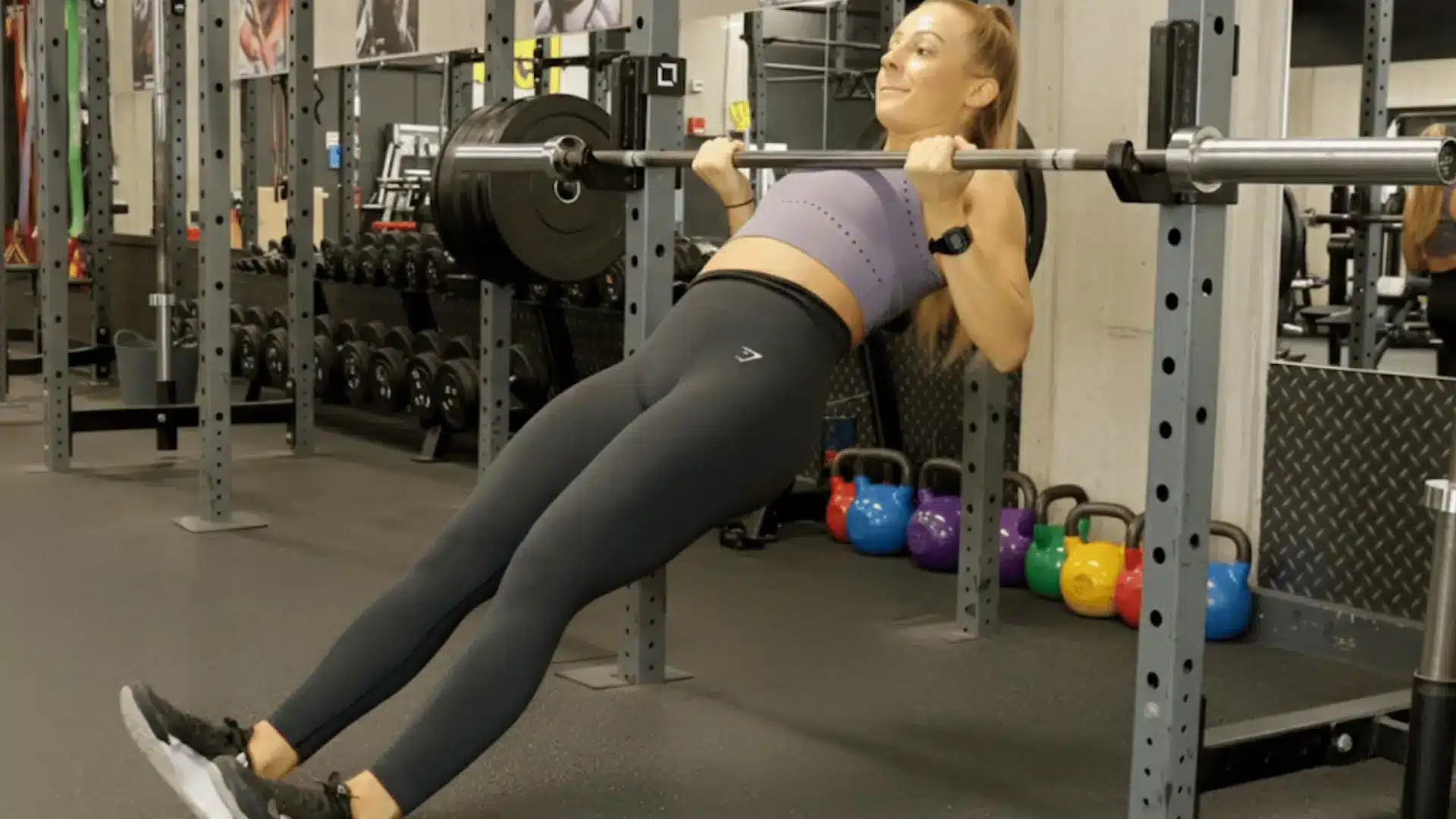 woman performing an inverted row under a barbell, keeping her body straight while pulling chest toward the bar