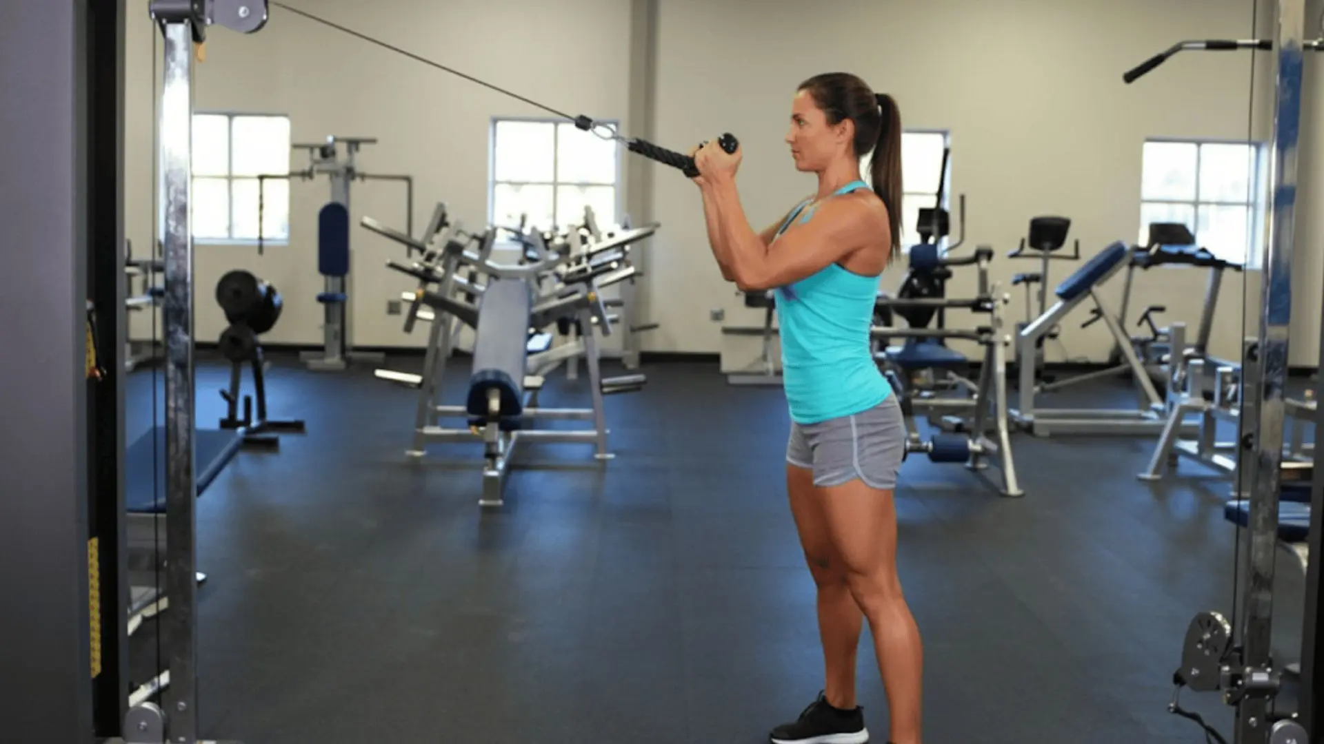 woman performing cable face pulls in a gym, pulling rope handles toward her face with elbows raised