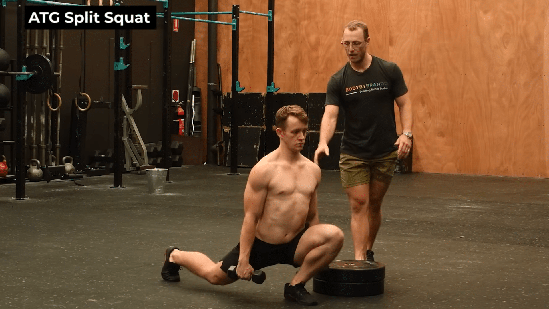 man performs a weighted atg Split Squat on flat ground, holding a dumbbell, as his coach provides feedback