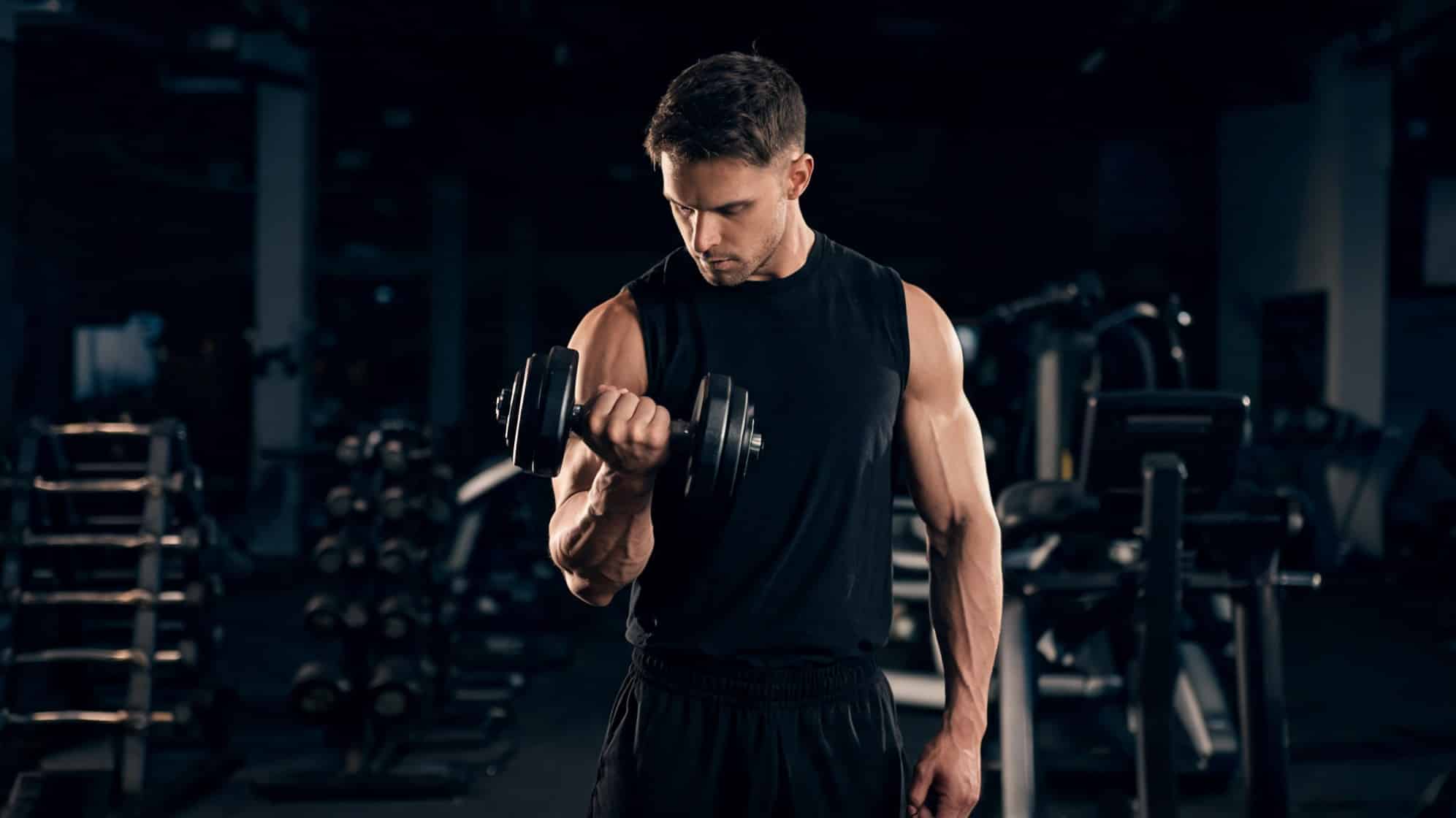 Man in a gym lifting a dumbbell with focus and intensity, surrounded by fitness equipment