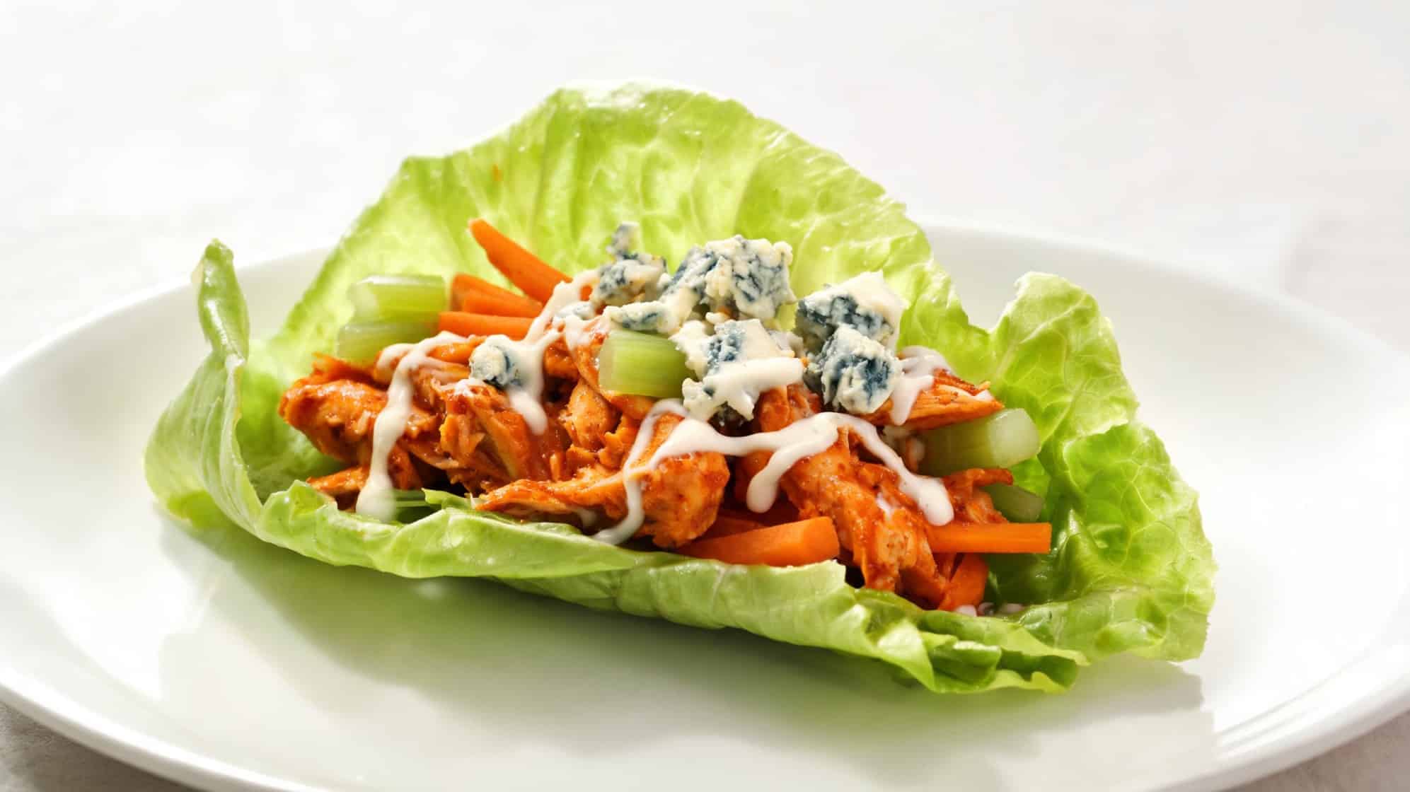 Lettuce wrap with shredded chicken, carrot sticks, celery, blue cheese, and drizzled dressing on a plate