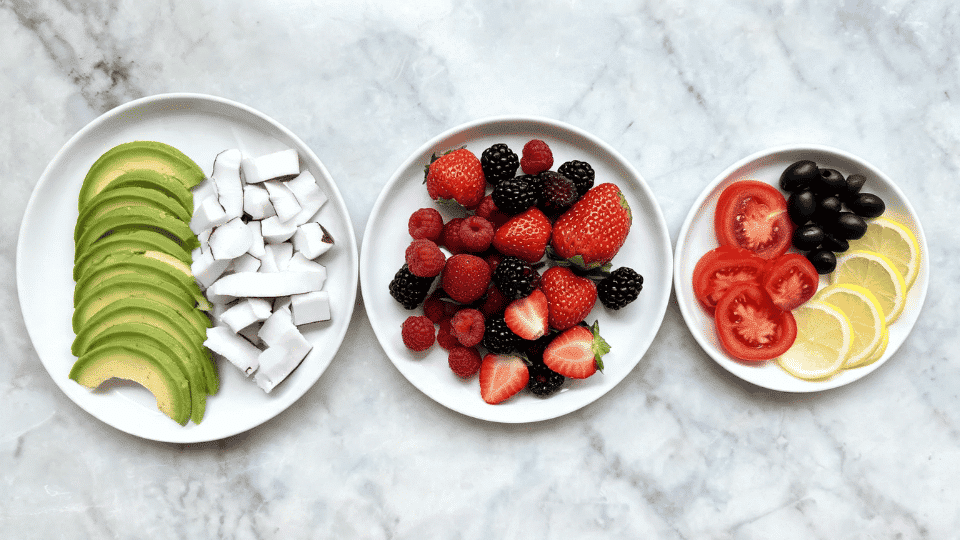 low sugar fruits including avocado raspberries blackberries strawberries coconut olives and lemon on a serving board