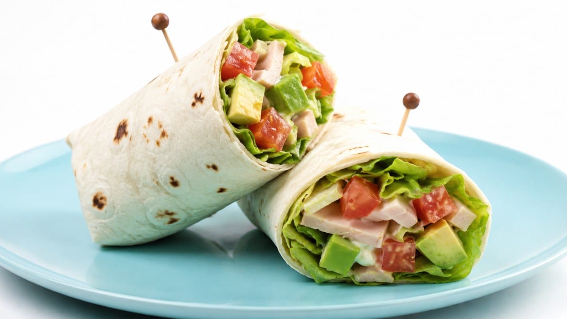 two tortilla wraps filled with lettuce, avocado, and turkey slices are pinned with toothpicks on a light blue plate