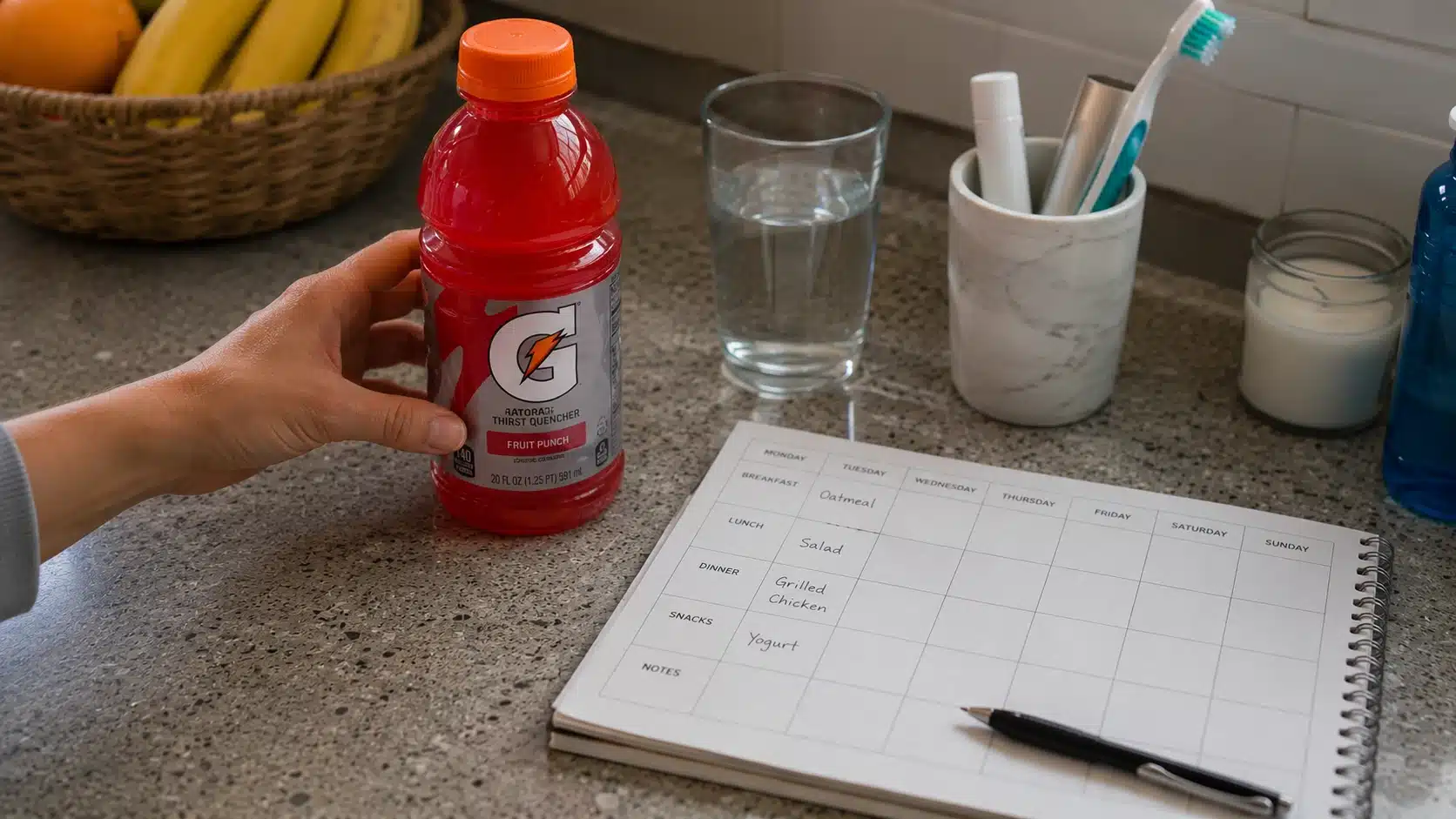 adult hand checking a gatorade label beside water planner and toothbrush cup at home