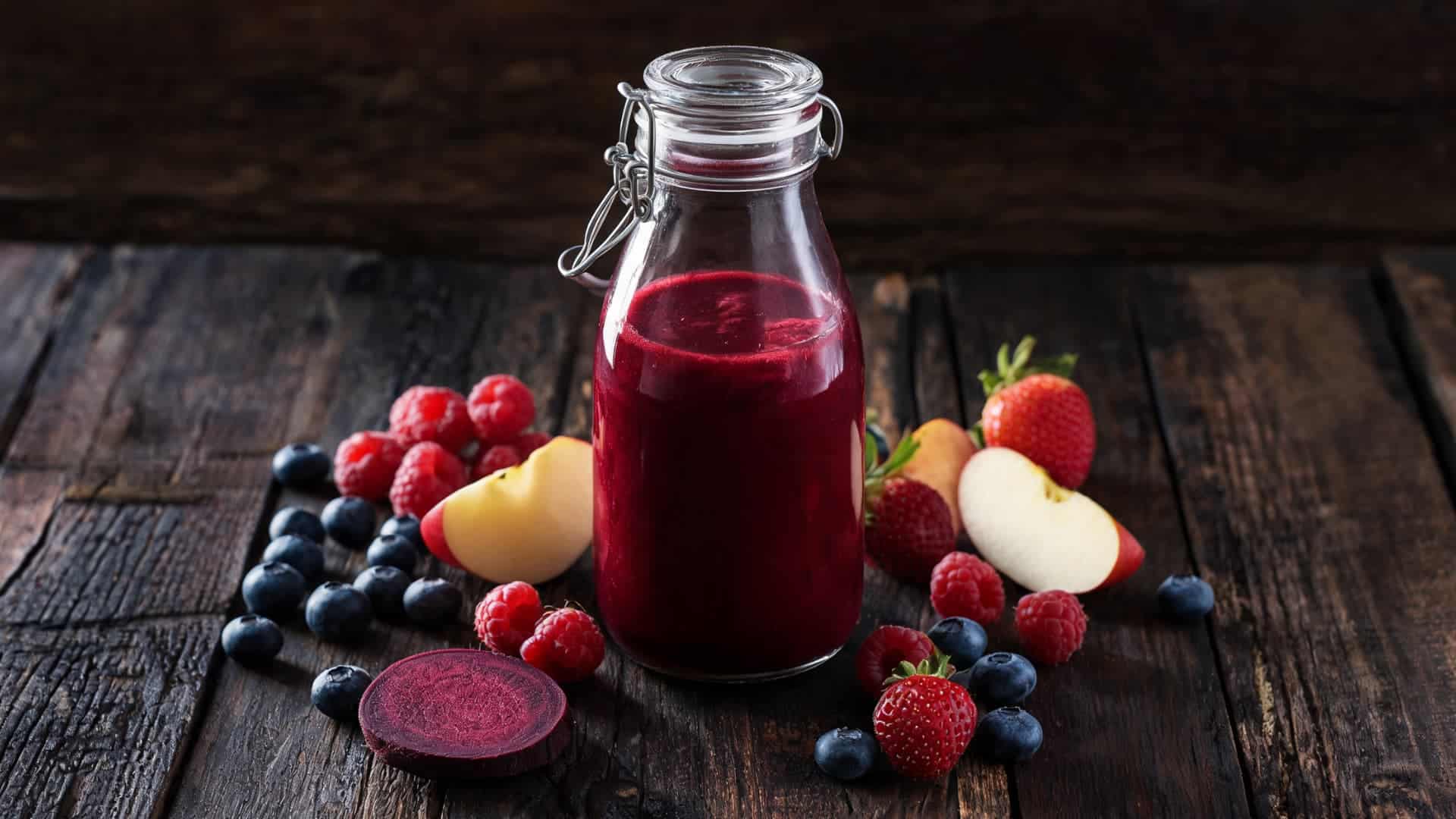 fresh mixed berry juice in glass bottle with strawberries blueberries raspberries and apples on wooden table