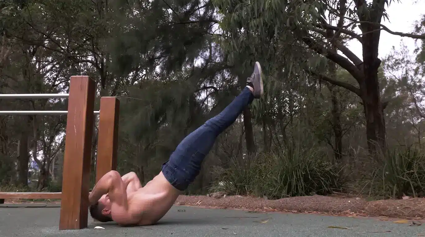 man performing a dragon flag outdoors with legs raised and body straight while gripping a wooden support