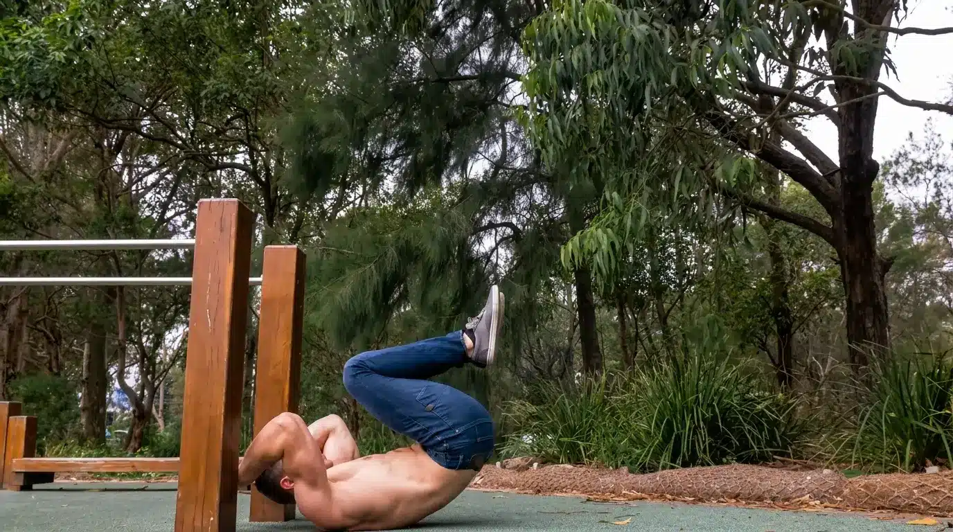 man practicing a tuck dragon flag outdoors while gripping a wooden support with knees bent and core engaged