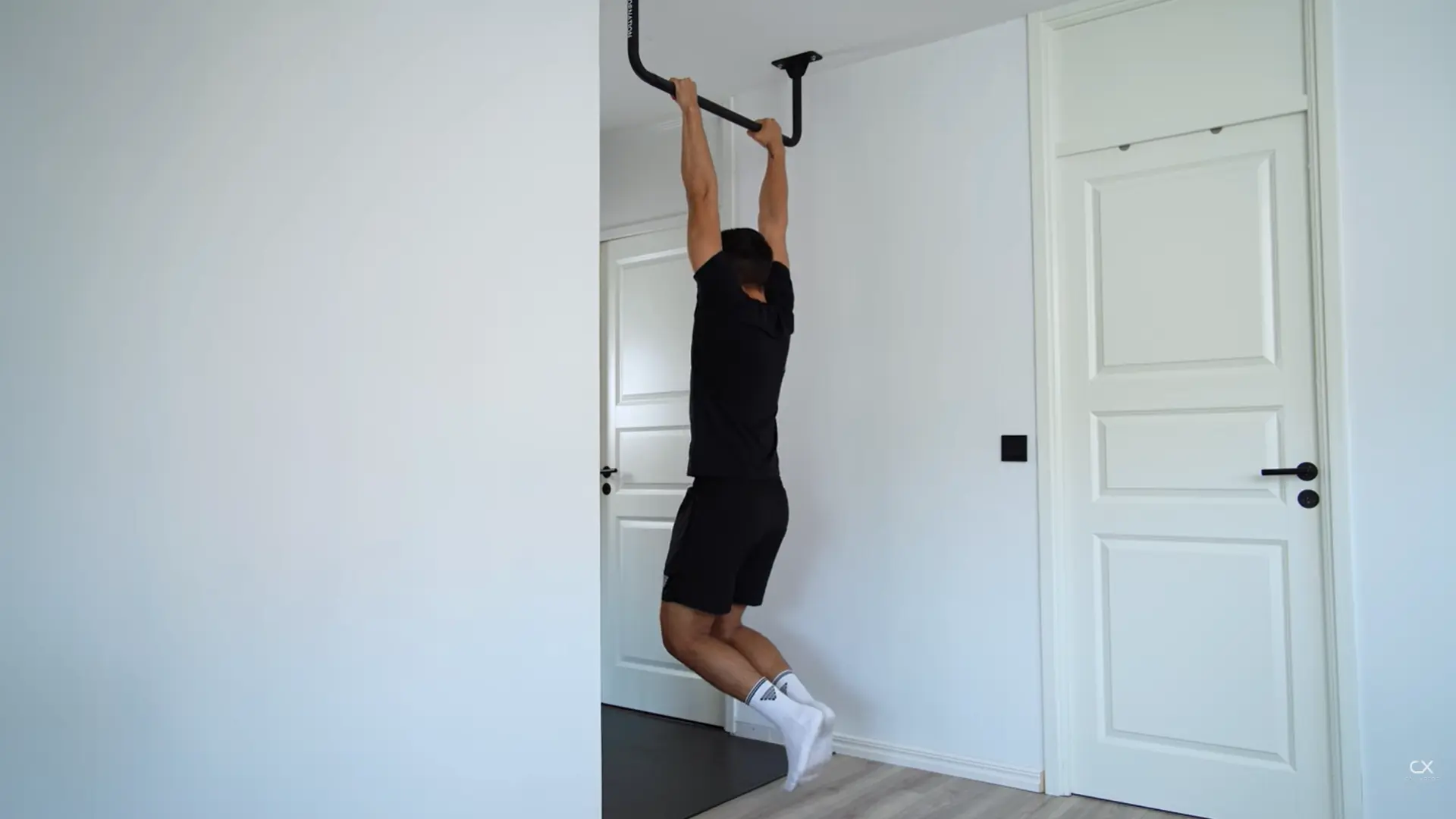 person hanging from a pull-up bar with arms fully extended, shoulders engaged but relaxed, and feet off the ground