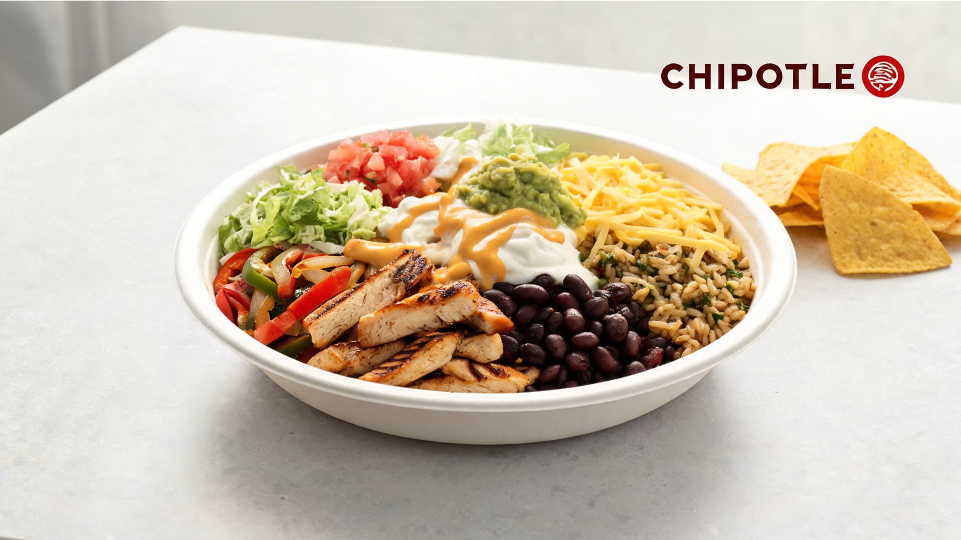 chipotle style burrito bowl with chicken rice beans salsa guacamole cheese sour cream queso and chips on a counter
