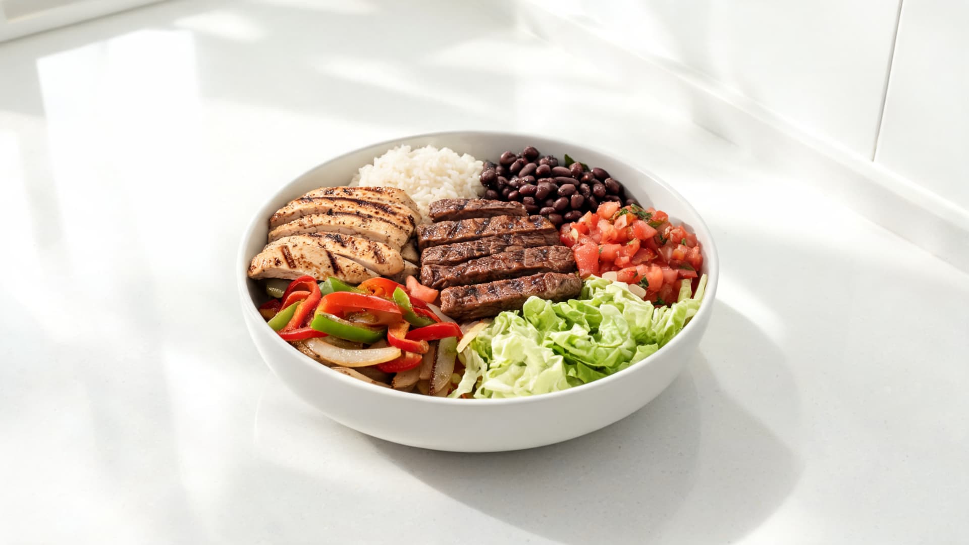 high protein burrito bowl with grilled chicken steak beans rice salsa lettuce and fajita vegetables on a bright counter